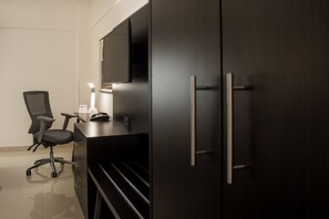 A modern office space with a dark wooden desk, a black office chair, and a flat-screen TV mounted on the wall.