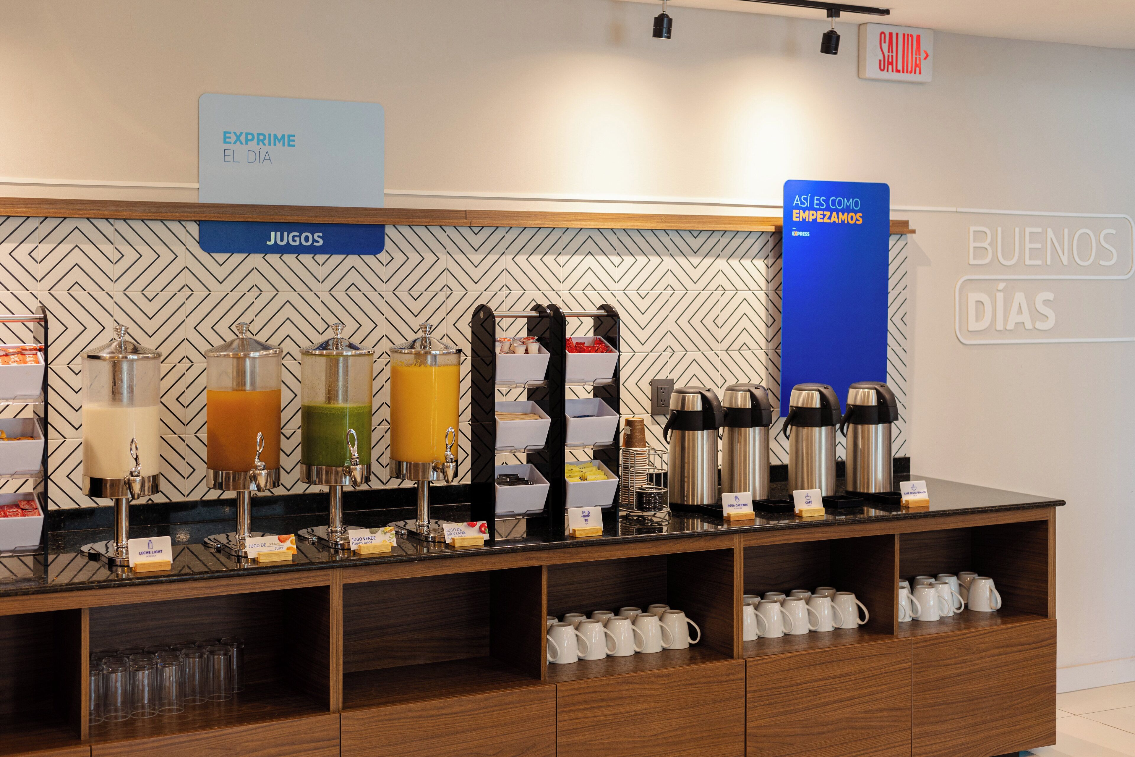 A breakfast bar with various juice dispensers, coffee makers, and mugs.