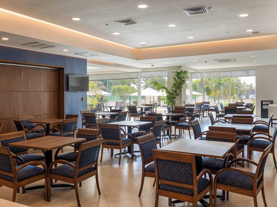 A spacious indoor dining area with multiple tables and chairs, large windows, and a view of the outdoors.