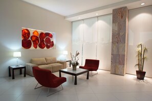 A modern living room with a sofa, two red chairs, a coffee table, and a large abstract painting on the wall.