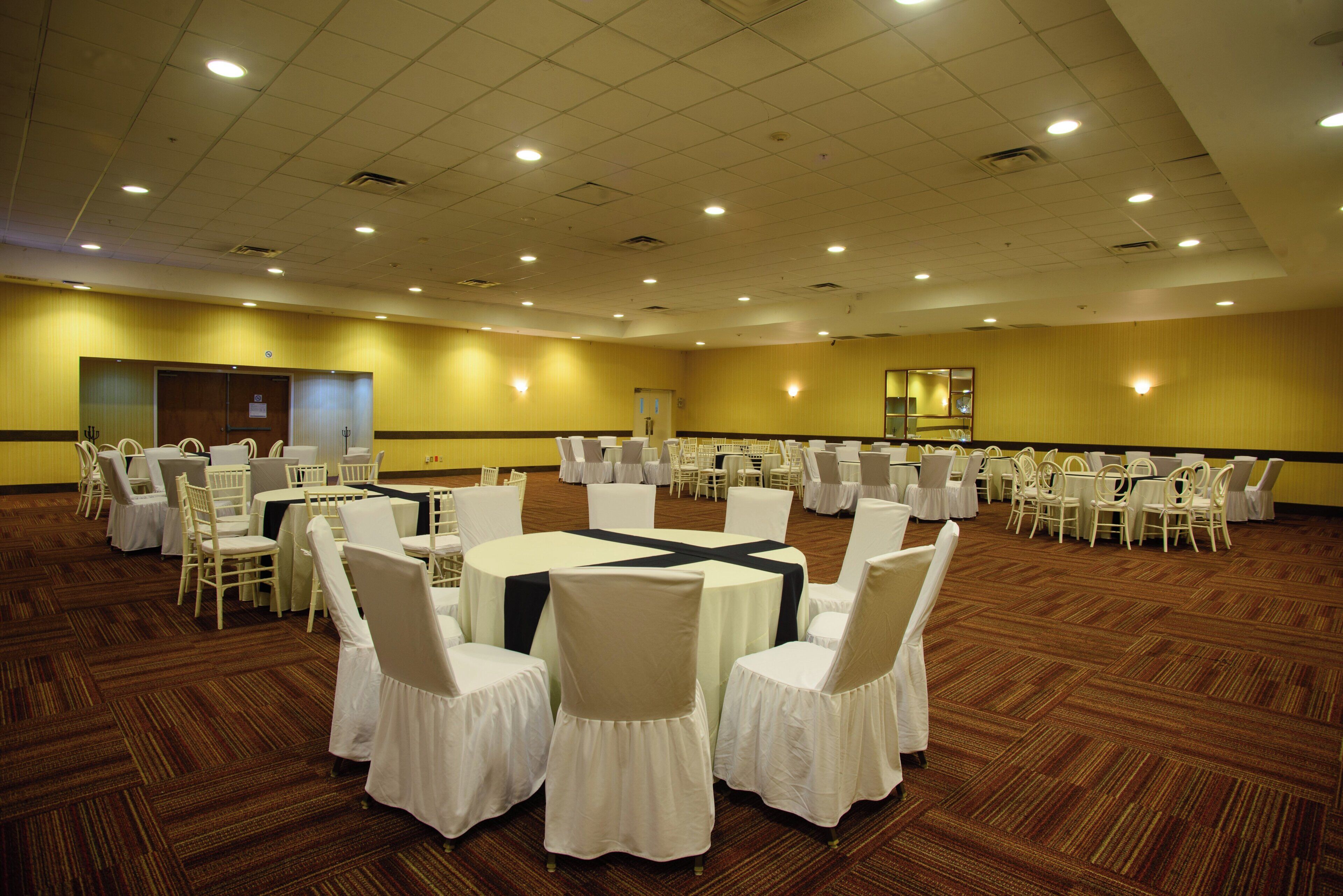 A large conference room with multiple round tables and chairs, carpeted flooring, and recessed lighting.