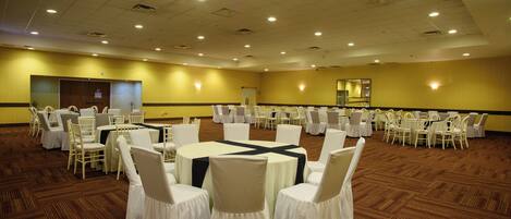 A large conference room with multiple round tables and chairs, carpeted flooring, and recessed lighting.