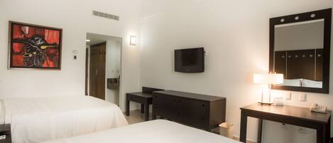 Habitación de hotel con dos camas, un escritorio, una cómoda, televisor, espejo y un cuadro en la pared.