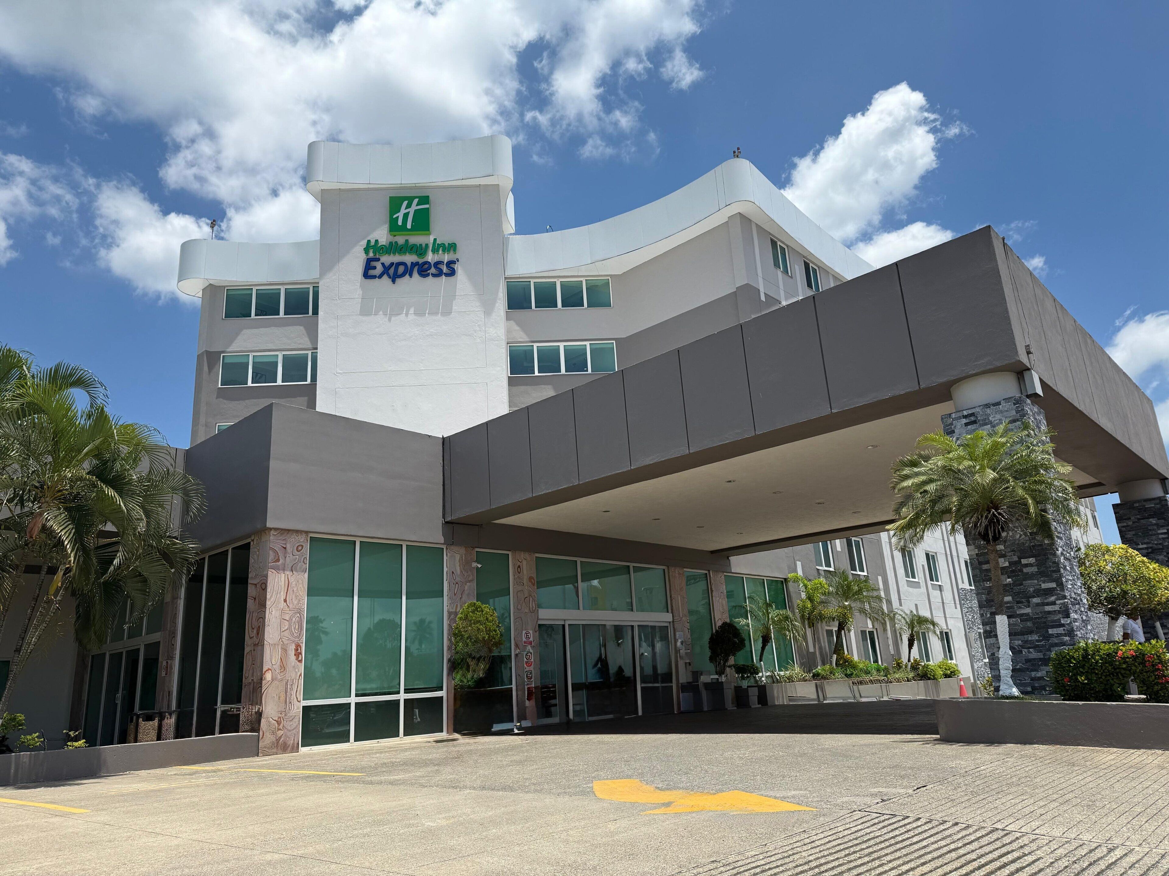 Un hotel Holiday Inn Express con diseño moderno, que cuenta con amplios ventanales y una zona de entrada cubierta.