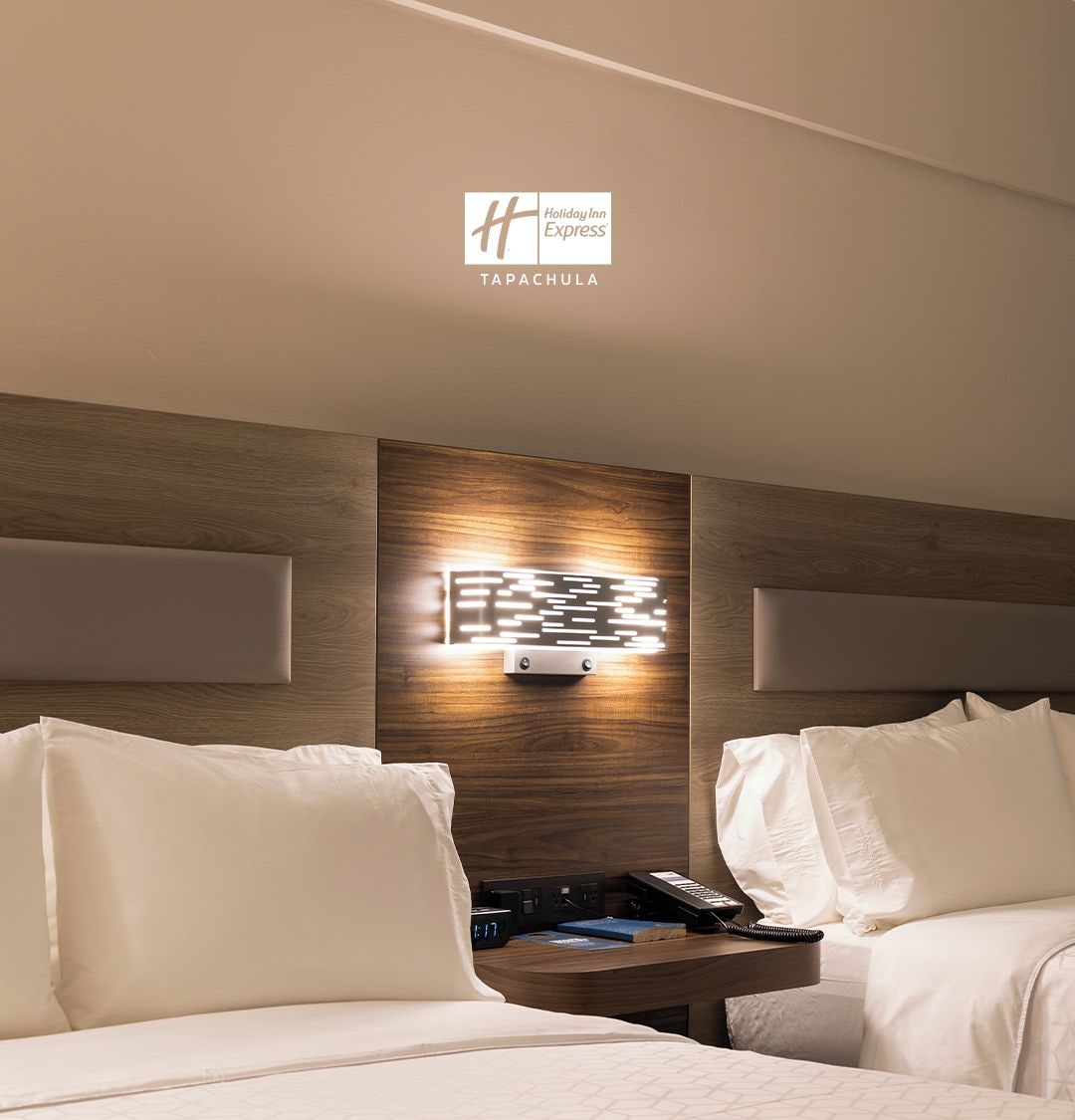Una habitación de hotel moderna con una pared de acento de madera, una mesita de noche con teléfono y reloj, y dos camas con ropa blanca.