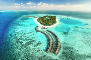 Vista aérea de un resort tropical con bungalows sobre el agua conectados por un paseo de madera.