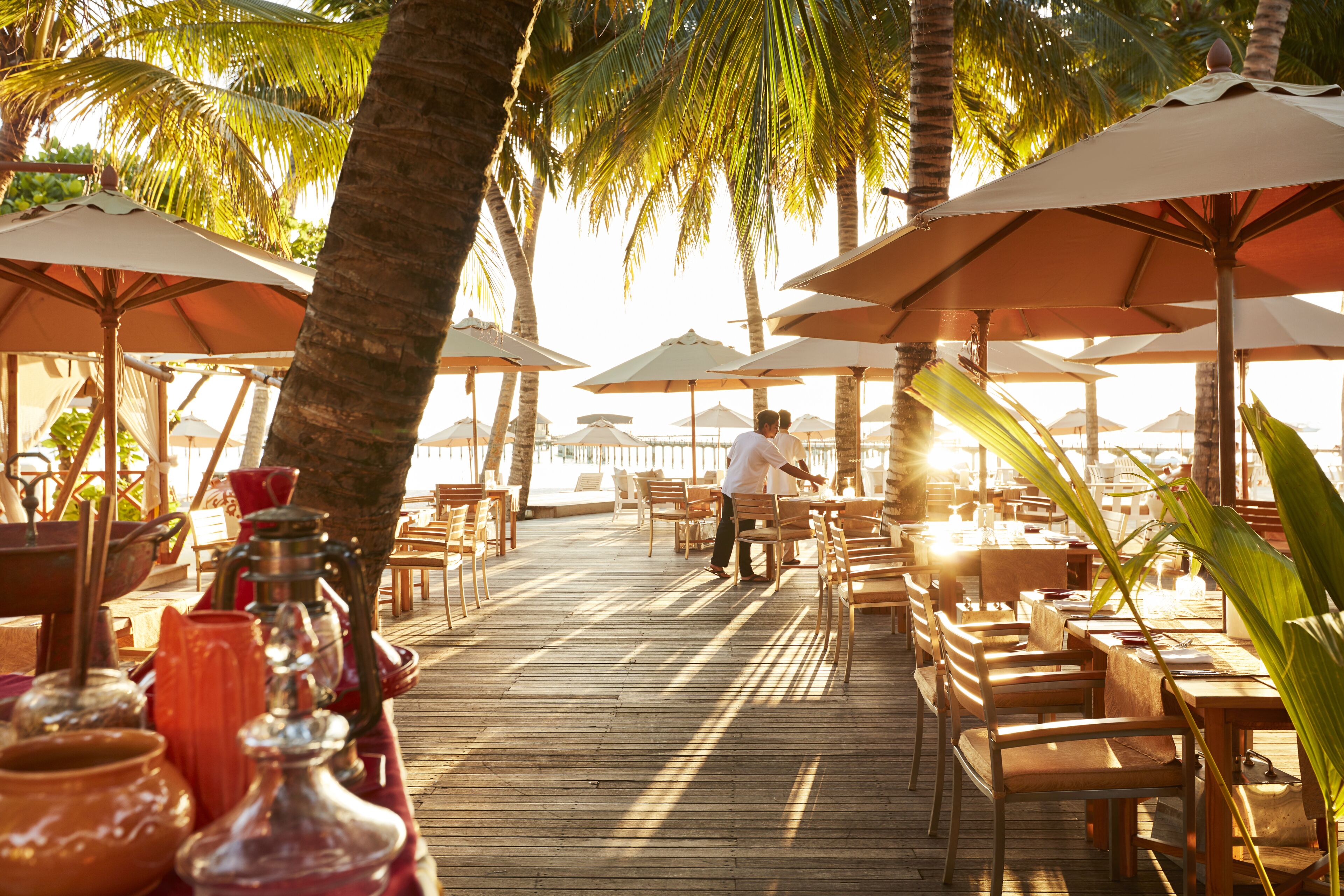 A wooden deck with outdoor seating and umbrellas, surrounded by palm trees.