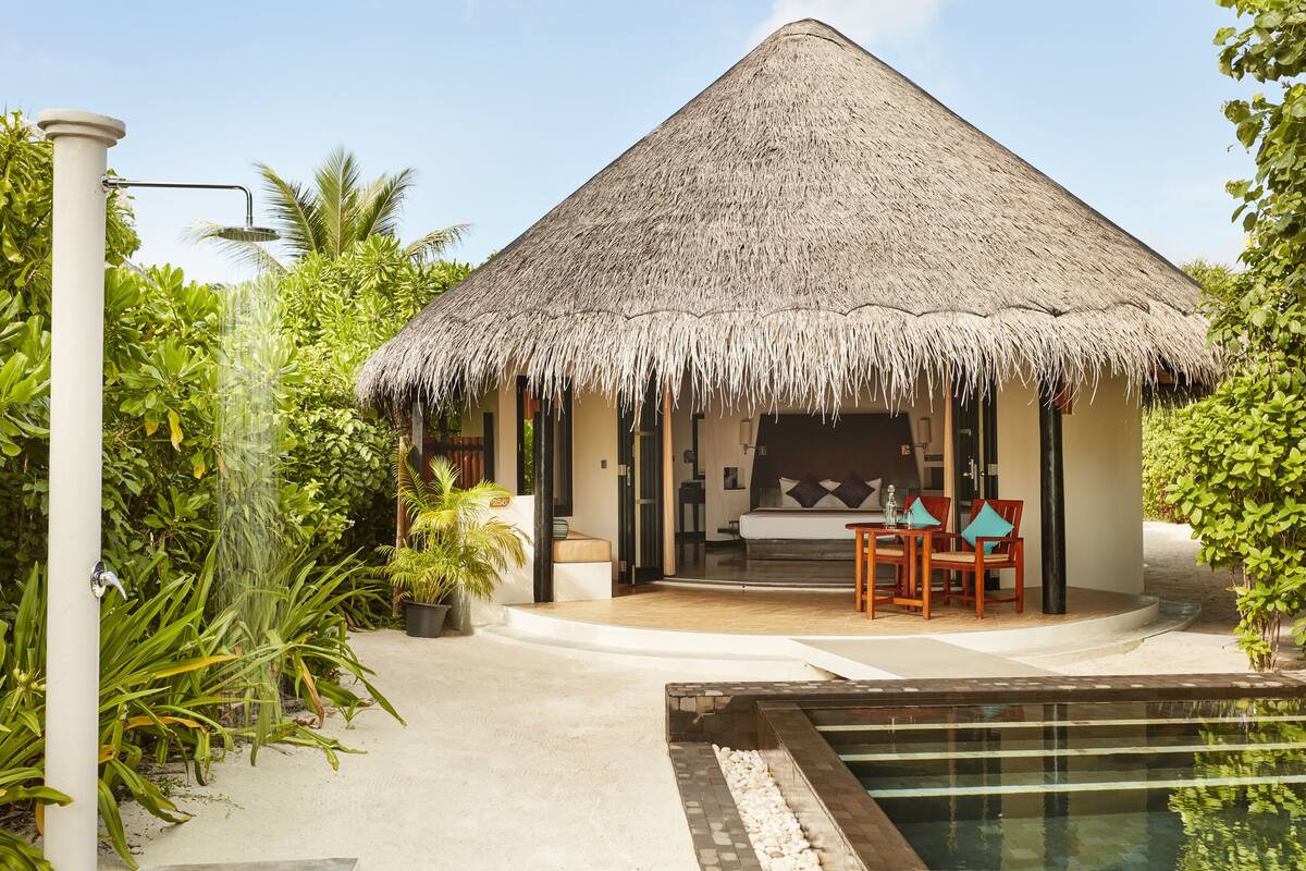 Une maison à toit de chaume avec une piscine et un espace extérieur aménagé pour se détendre.