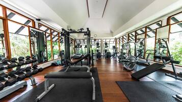 Un gimnasio con diferentes equipos de ejercicio, pisos de madera y ventanas amplias que dan a zonas verdes.