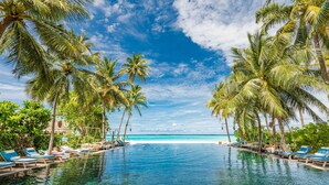 A clear blue pool with lounge chairs and palm trees, leading to a beach. - Sun Siyam Iru Fushi (Iru Fushi)