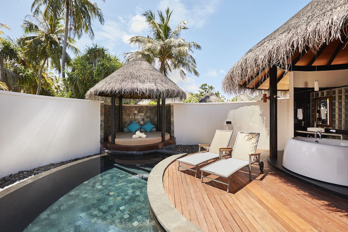 A pool area with lounge chairs, a hot tub, and a thatched-roof structure.