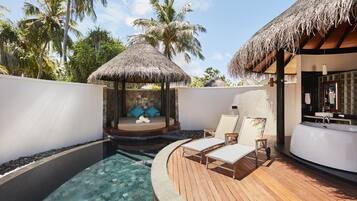 A pool area with lounge chairs, a hot tub, and a thatched-roof structure.