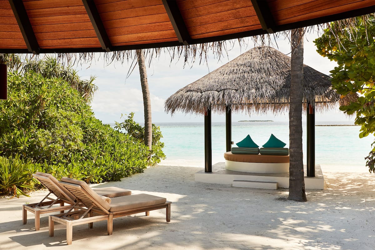 A beachside lounge with wooden chairs and a thatched-roof gazebo overlooking the sea.