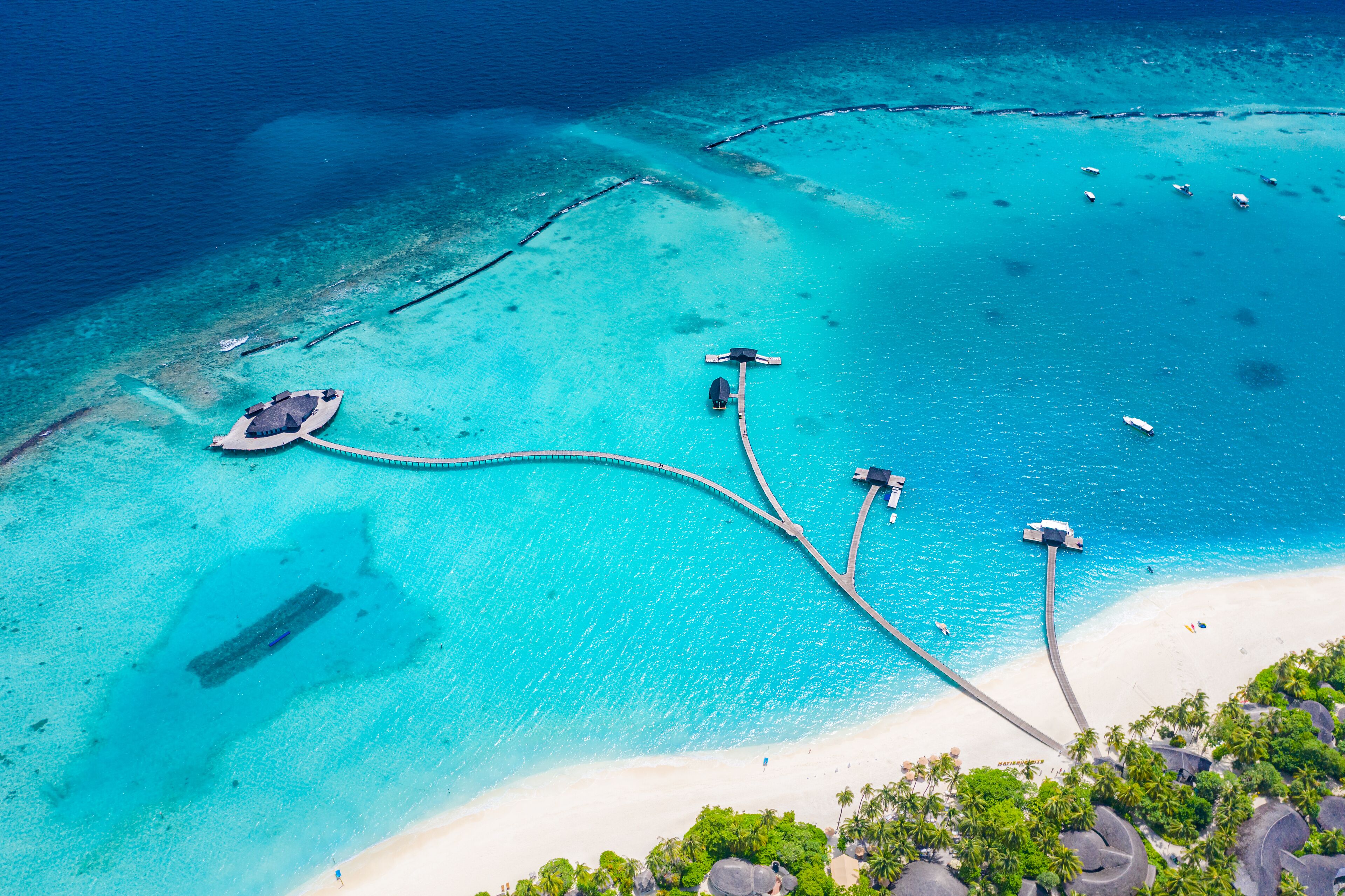 Vista aérea de um resort na praia, com águas turquesa cristalinas, uma faixa de areia e uma pequena área de cais.