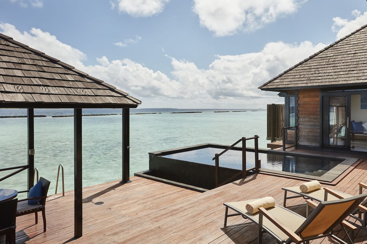 A wooden deck with a glass-bottomed infinity pool, lounge chairs, and a view of the ocean.