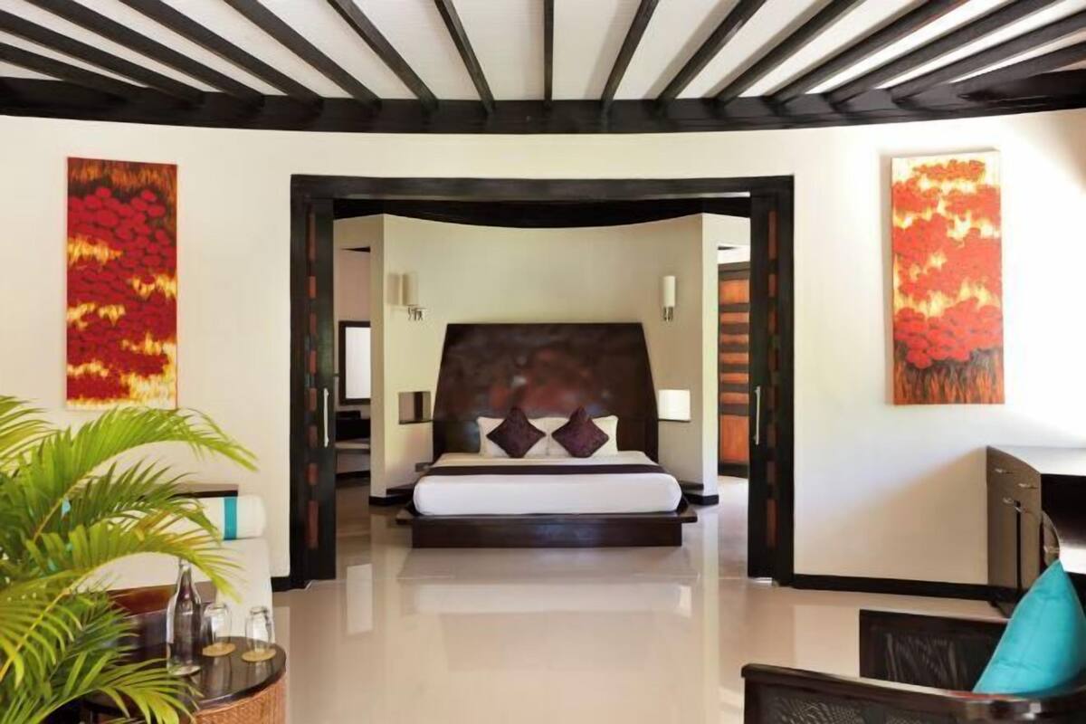 A modern hotel room with a large bed, a wooden ceiling, and two abstract paintings on the walls.