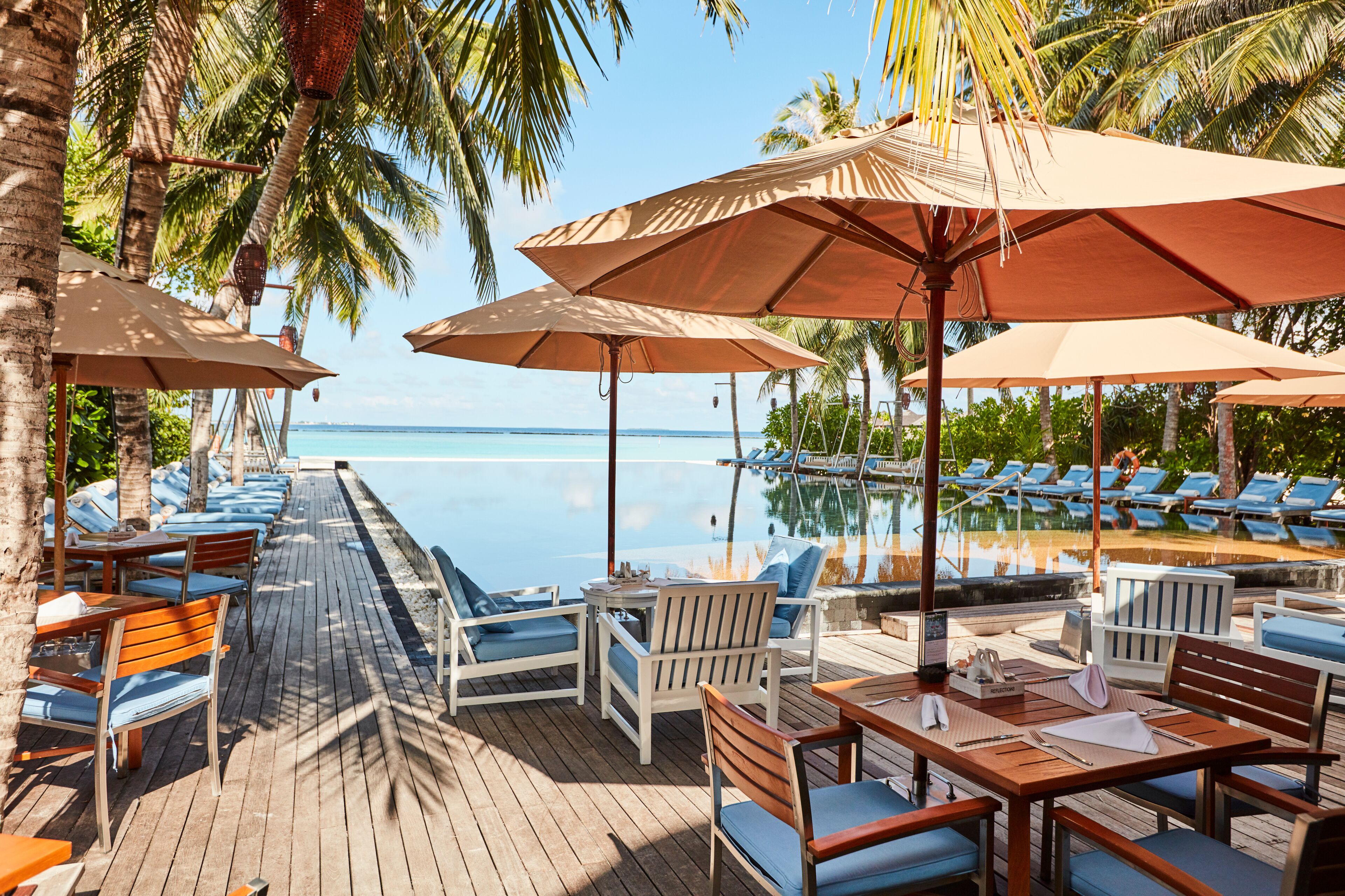A wooden deck with lounge chairs and umbrellas overlooking a pool and ocean.