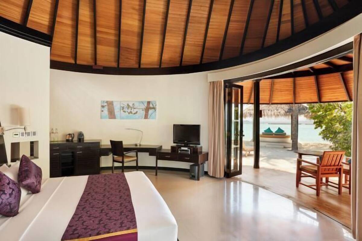 A hotel room with a bed, desk, TV, and a view of the beach.