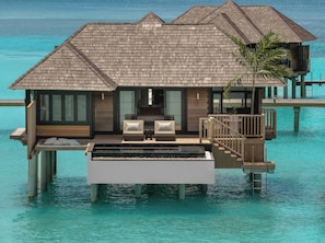 A luxurious overwater bungalow with a wooden exterior, a pool, and two sofas with cushions.