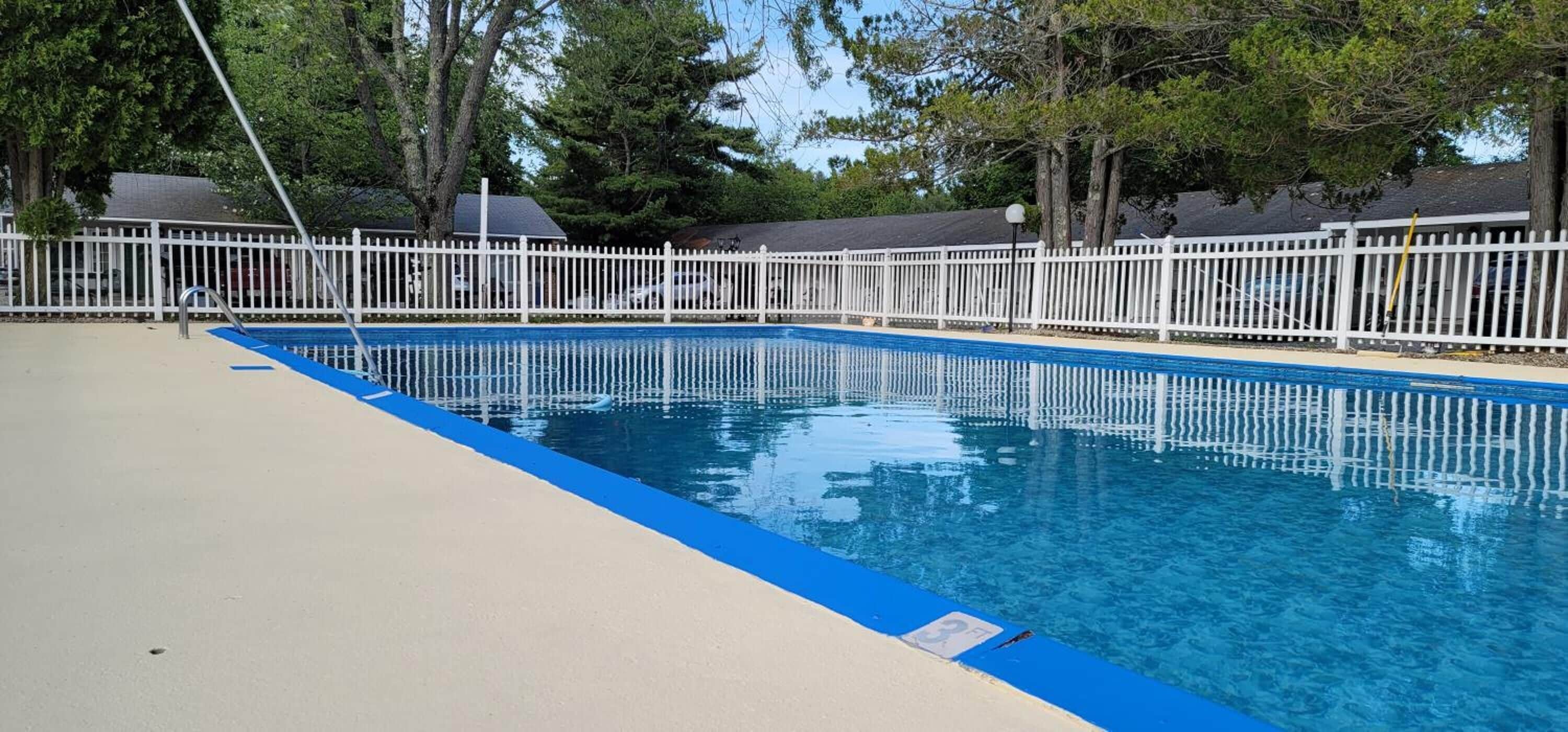 A swimming pool with a white fence, surrounded by trees and a clear sky.