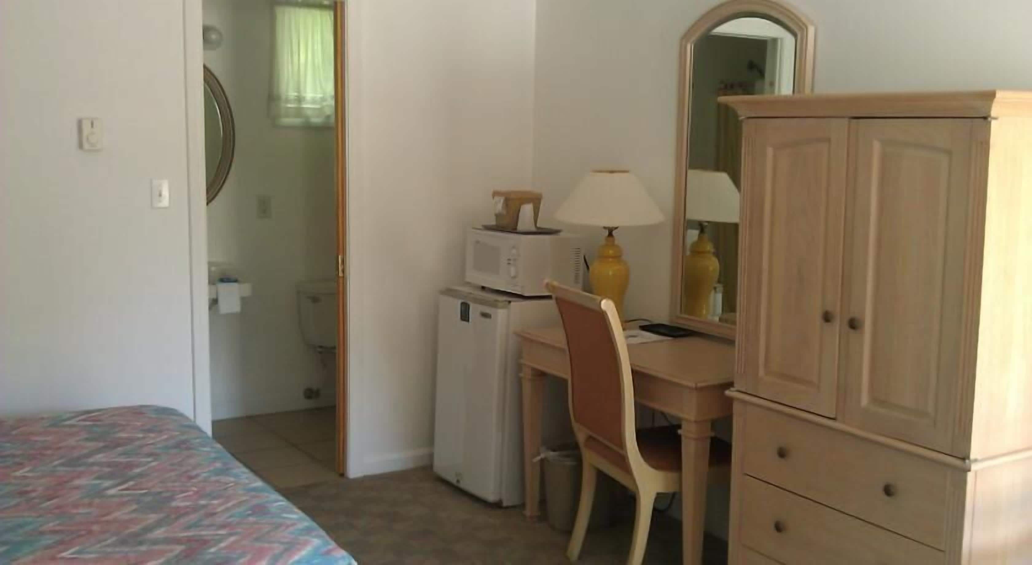 Une petite chambre à coucher, bien rangée, avec un lit, un bureau, une chaise, une armoire et un miroir.