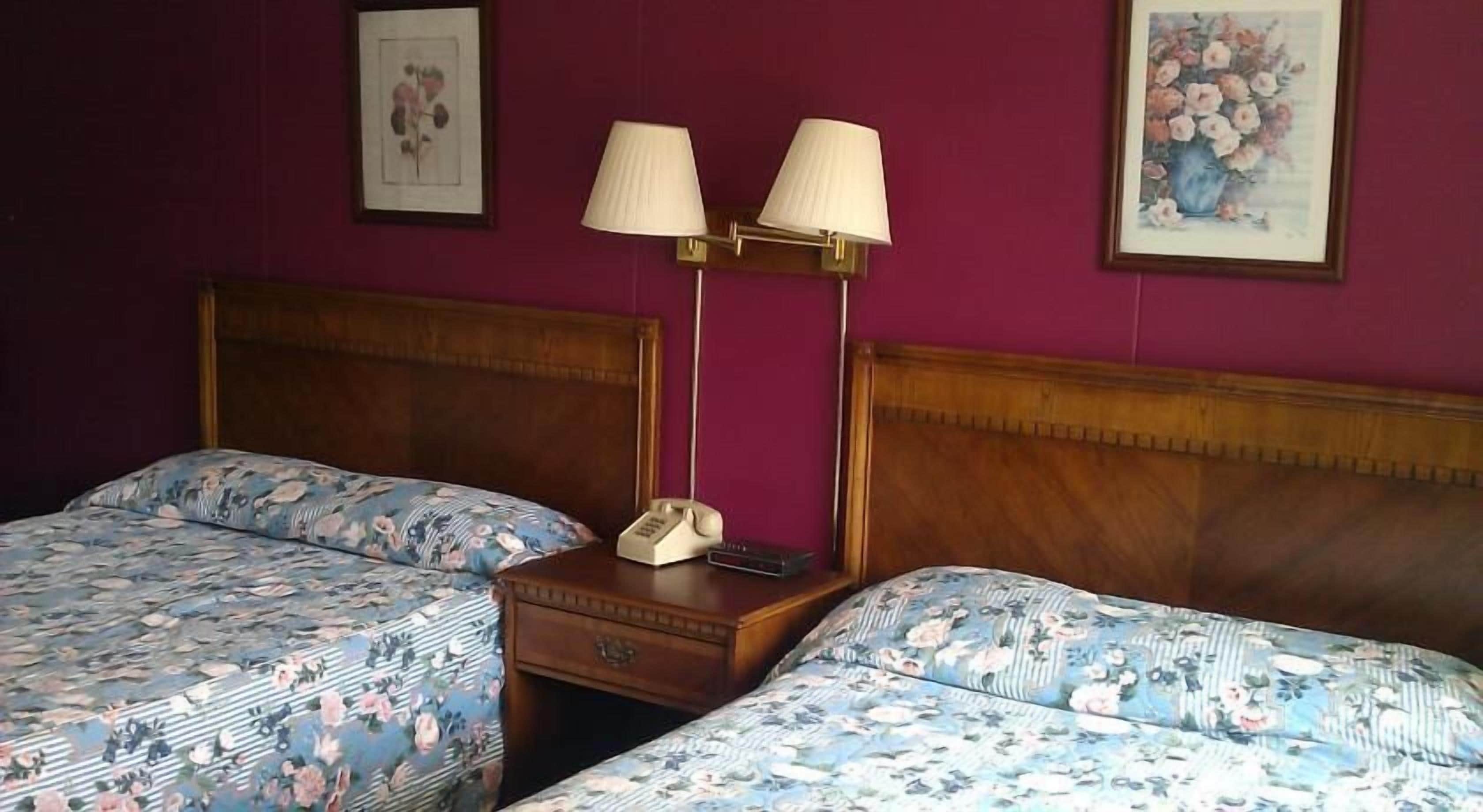 A hotel room with two beds, a nightstand with a lamp, and a telephone.