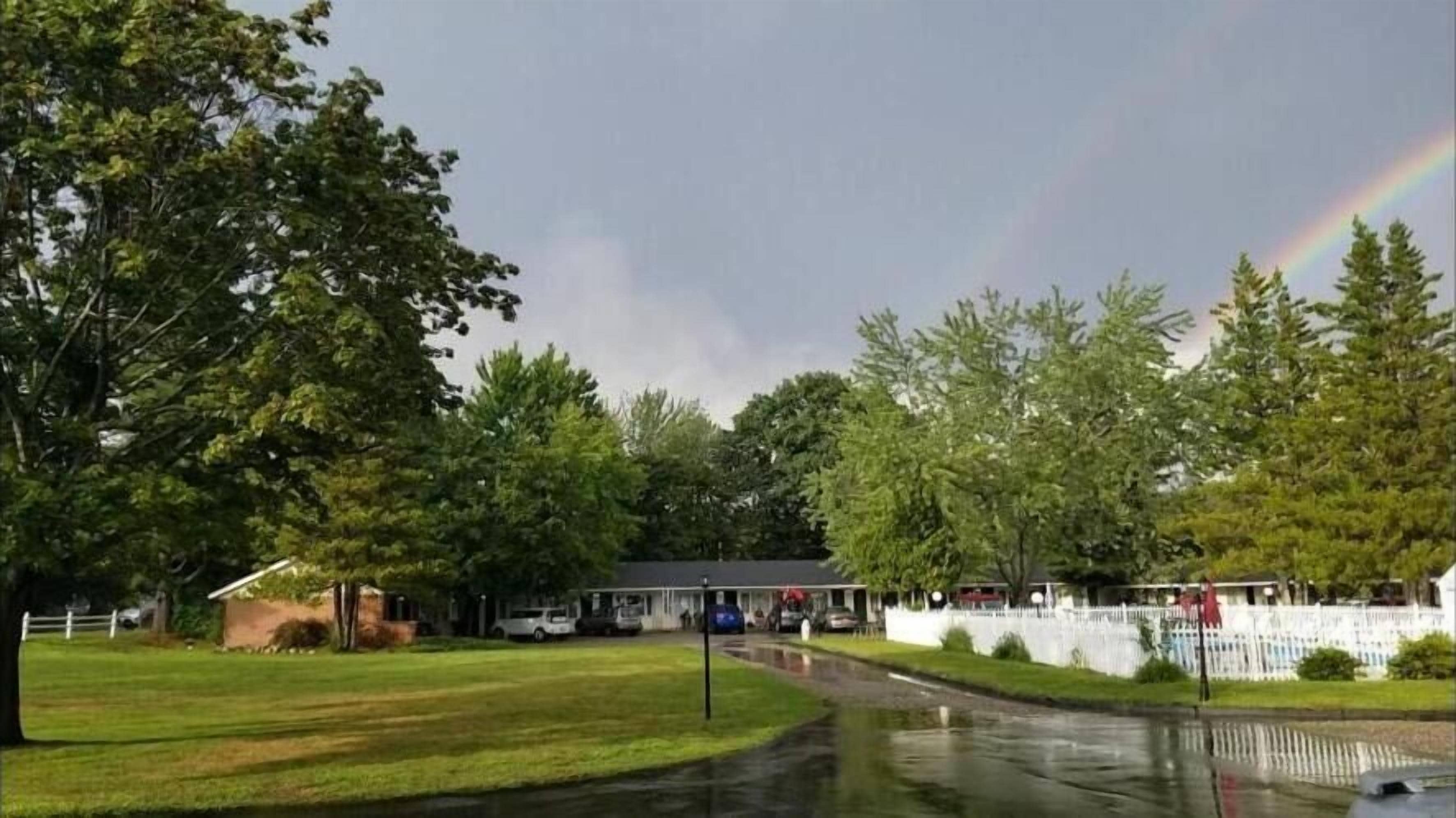 A residential area with a house, a white fence, and a rainbow in the sky.