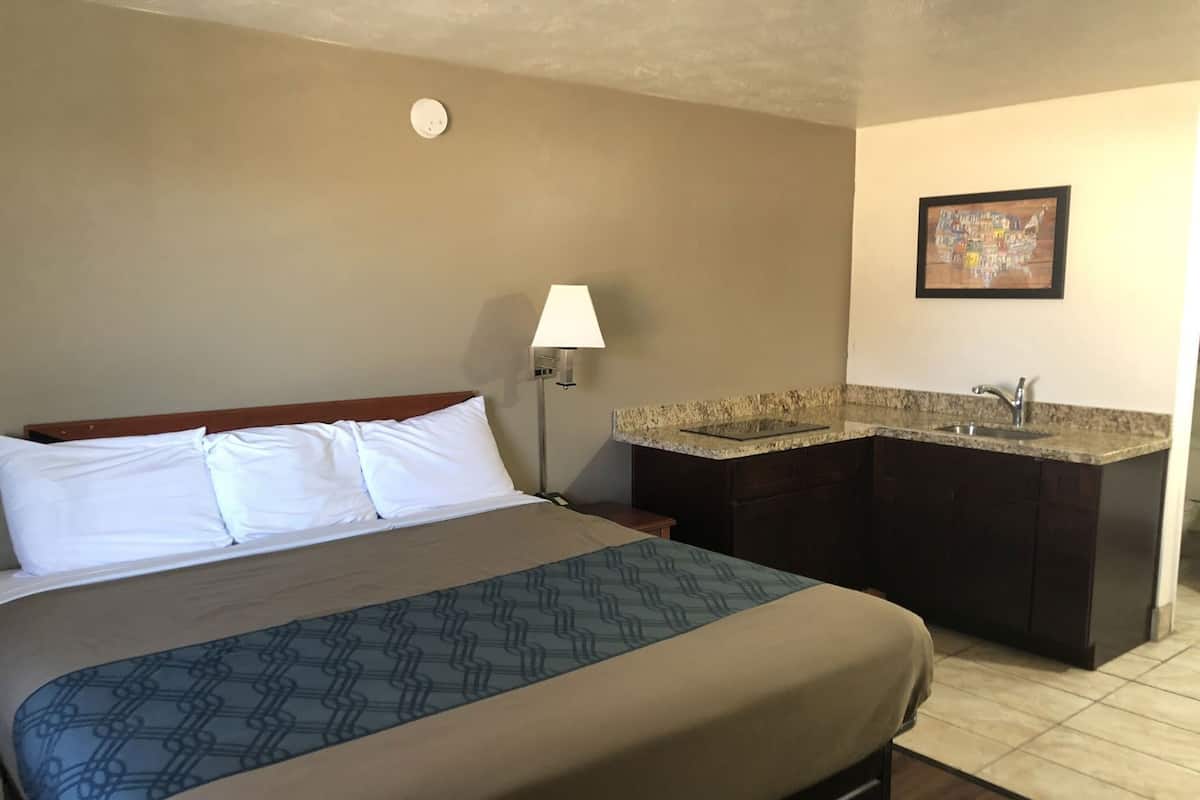 A hotel room with a bed, a nightstand, a lamp, a sink, and a framed map on the wall.