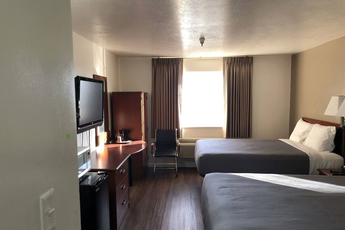 A hotel room with two beds, a desk with a television, a chair, and a window with curtains.