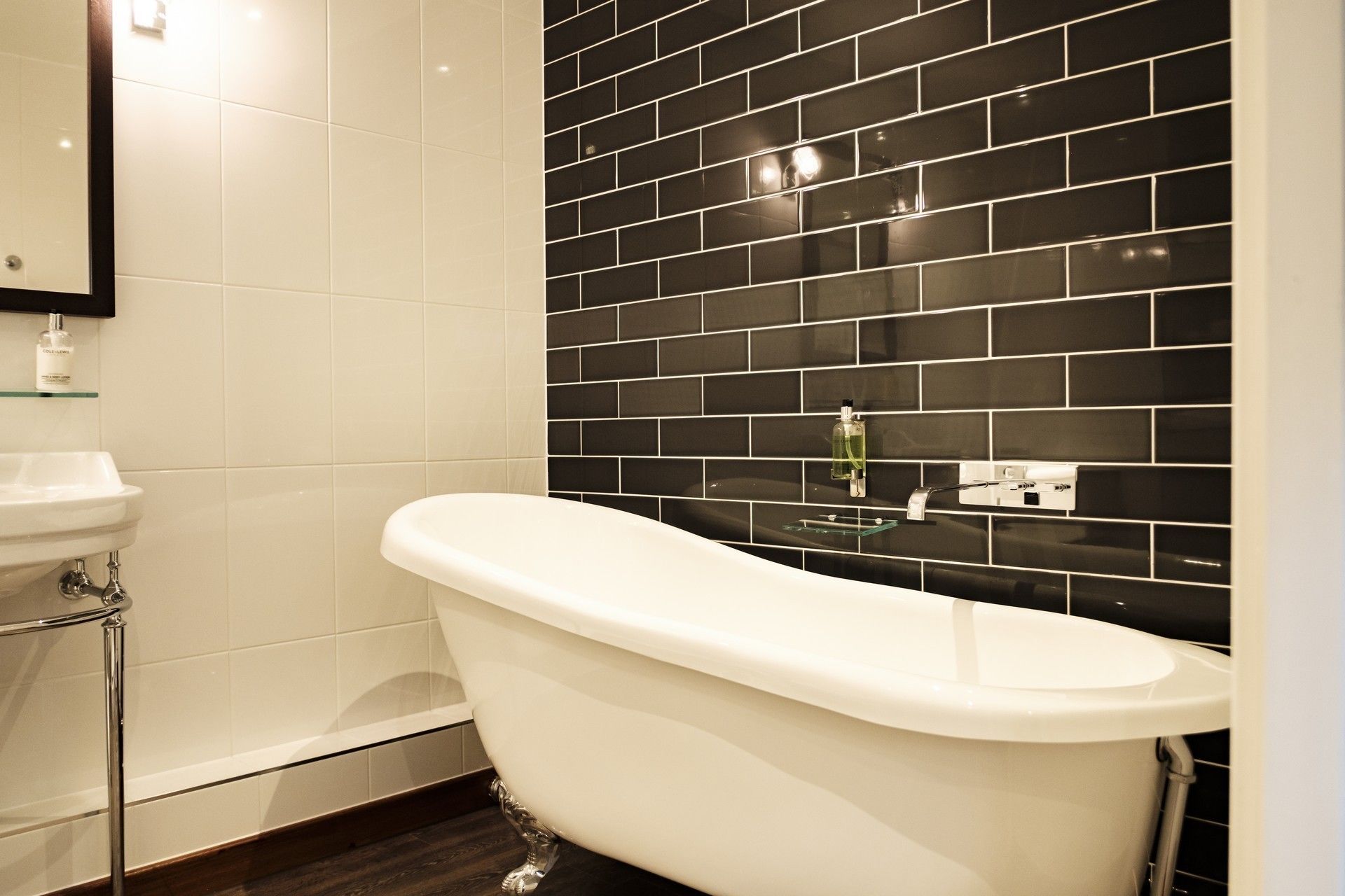 Une salle de bain avec une baignoire sur pieds, un lavabo blanc et un mur recouvert de carreaux noirs.