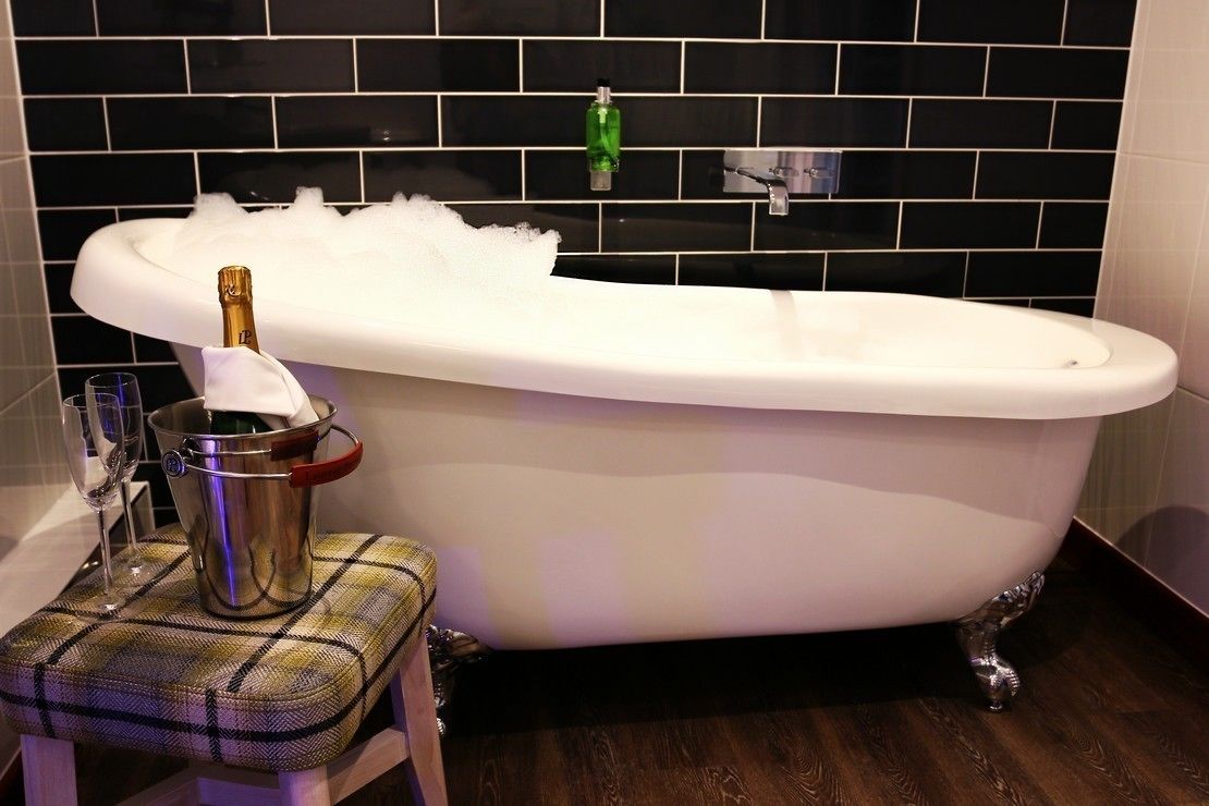 A bathroom with a freestanding bathtub, a glass of champagne, and a bottle of champagne on a stool.