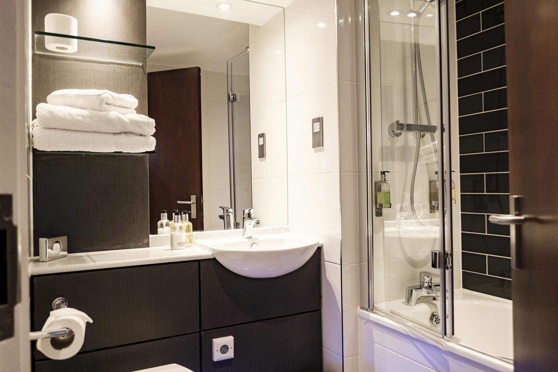 Une salle de bain moderne avec une douche à parois de verre, un lavabo avec un miroir au-dessus et des serviettes soigneusement pliées.