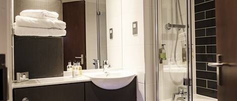 A modern bathroom with a glass shower enclosure, a sink with a mirror above, and neatly stacked towels.