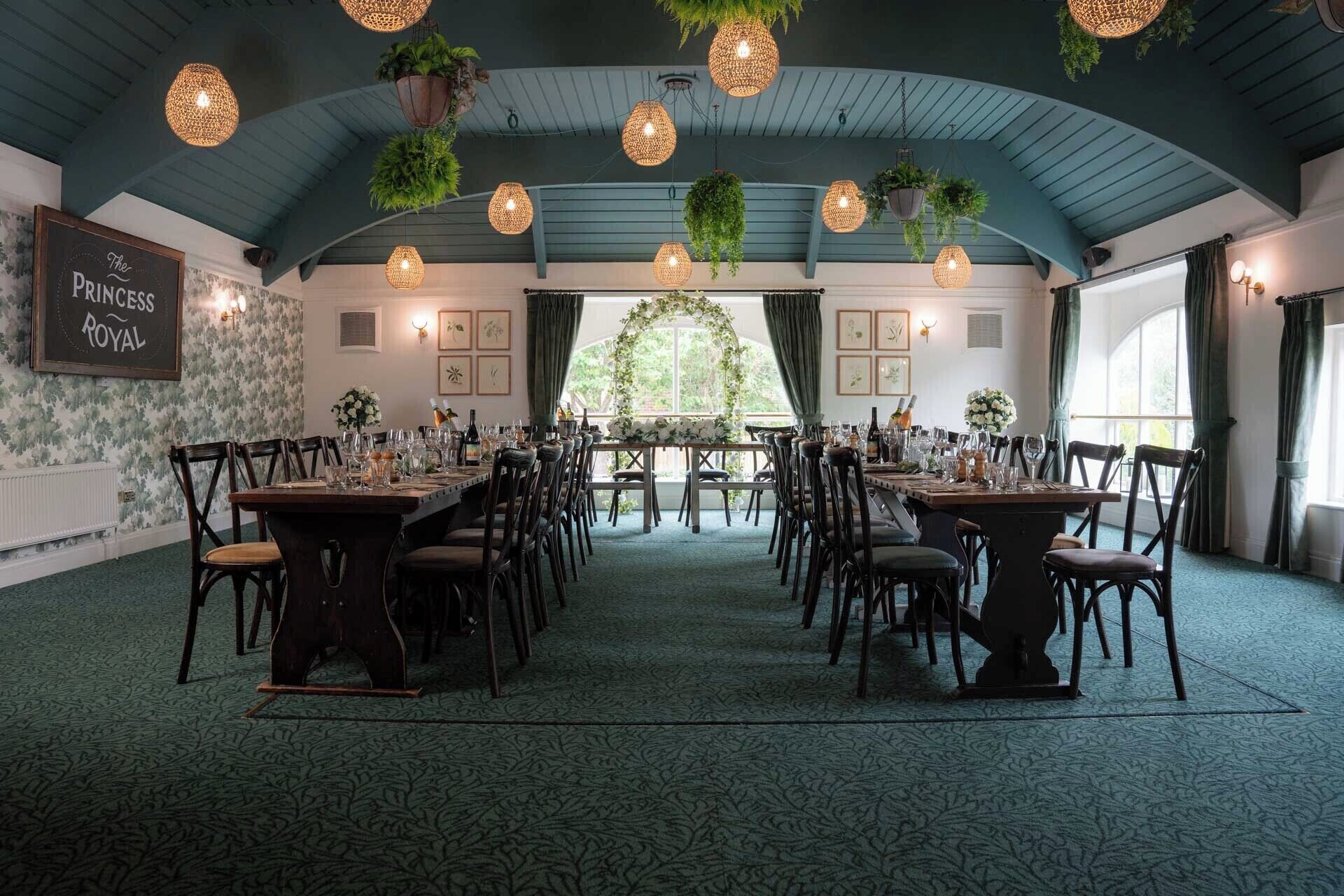 Un salón de banquetes con largas mesas dispuestas para comer, plantas colgantes y un letrero que dice "The Princess Royal".