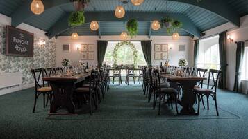 Un salón de banquetes con largas mesas dispuestas para comer, plantas colgantes y un letrero que dice "The Princess Royal".