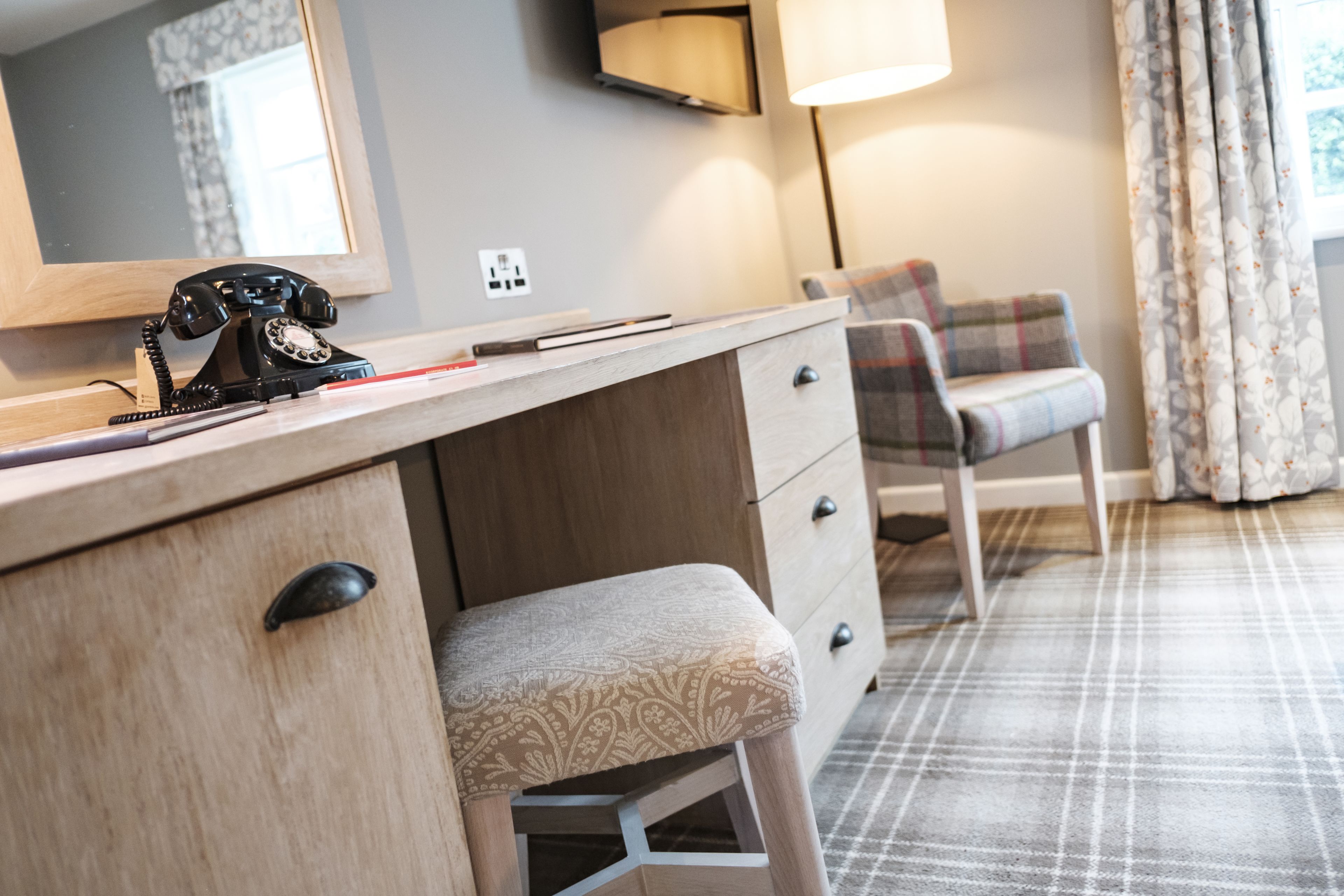 A hotel room with a wooden desk, a telephone, a chair, and a lamp.