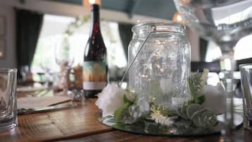Una mesa con un tarro de vidrio que contiene flores y follaje, una botella de vino y copas.