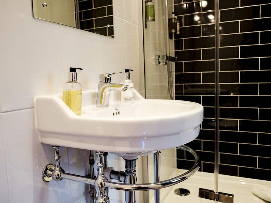 Un baño con lavamanos blanco, dos botellas de jabón líquido y un grifo cromado.