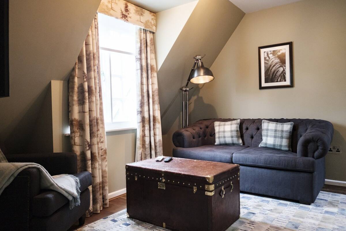 Ein Wohnzimmer mit einem dunkelblauen Sofa, einem braunen Koffer und einer Lampe.