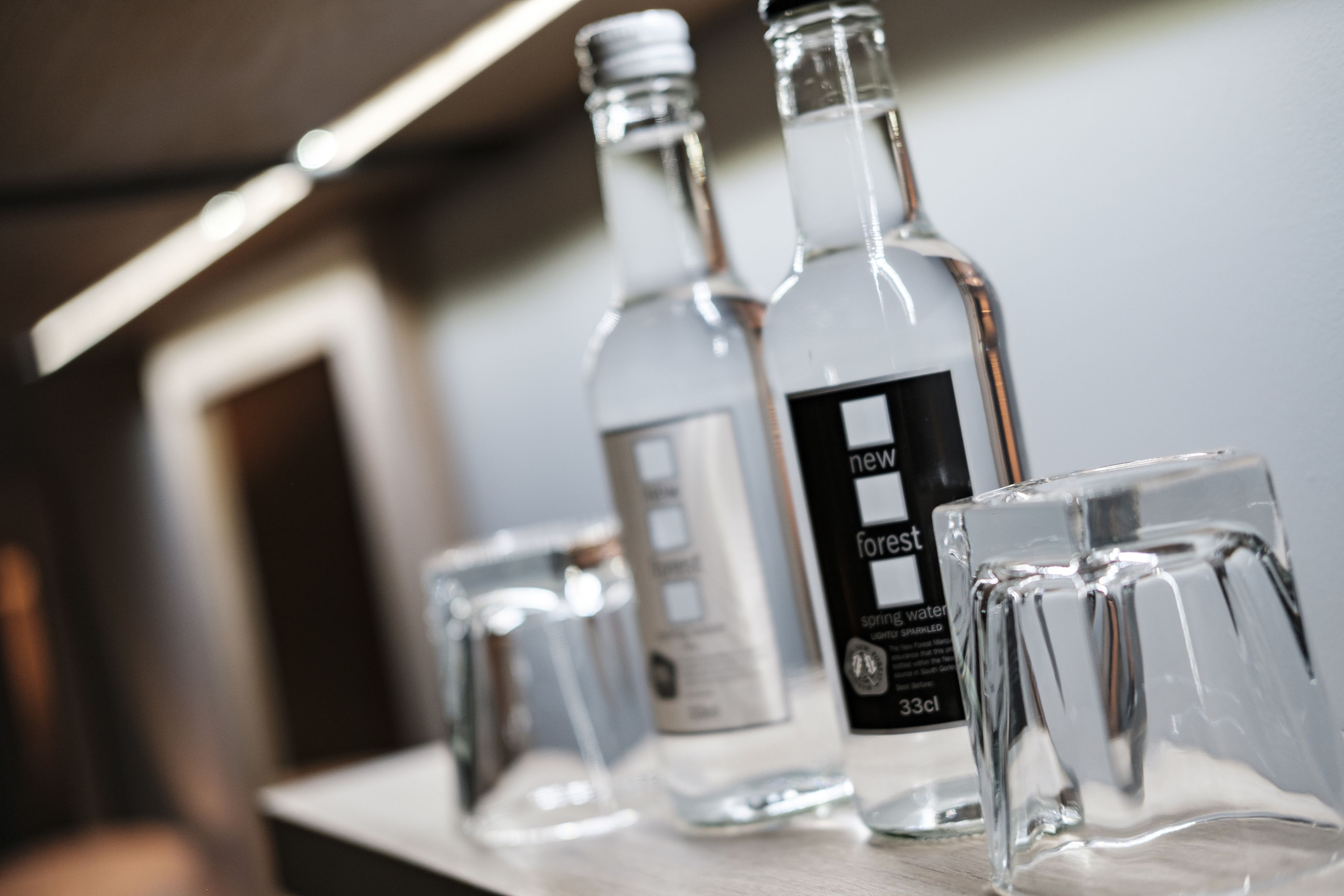Uma área de bar com garrafas e copos de vidro transparente.