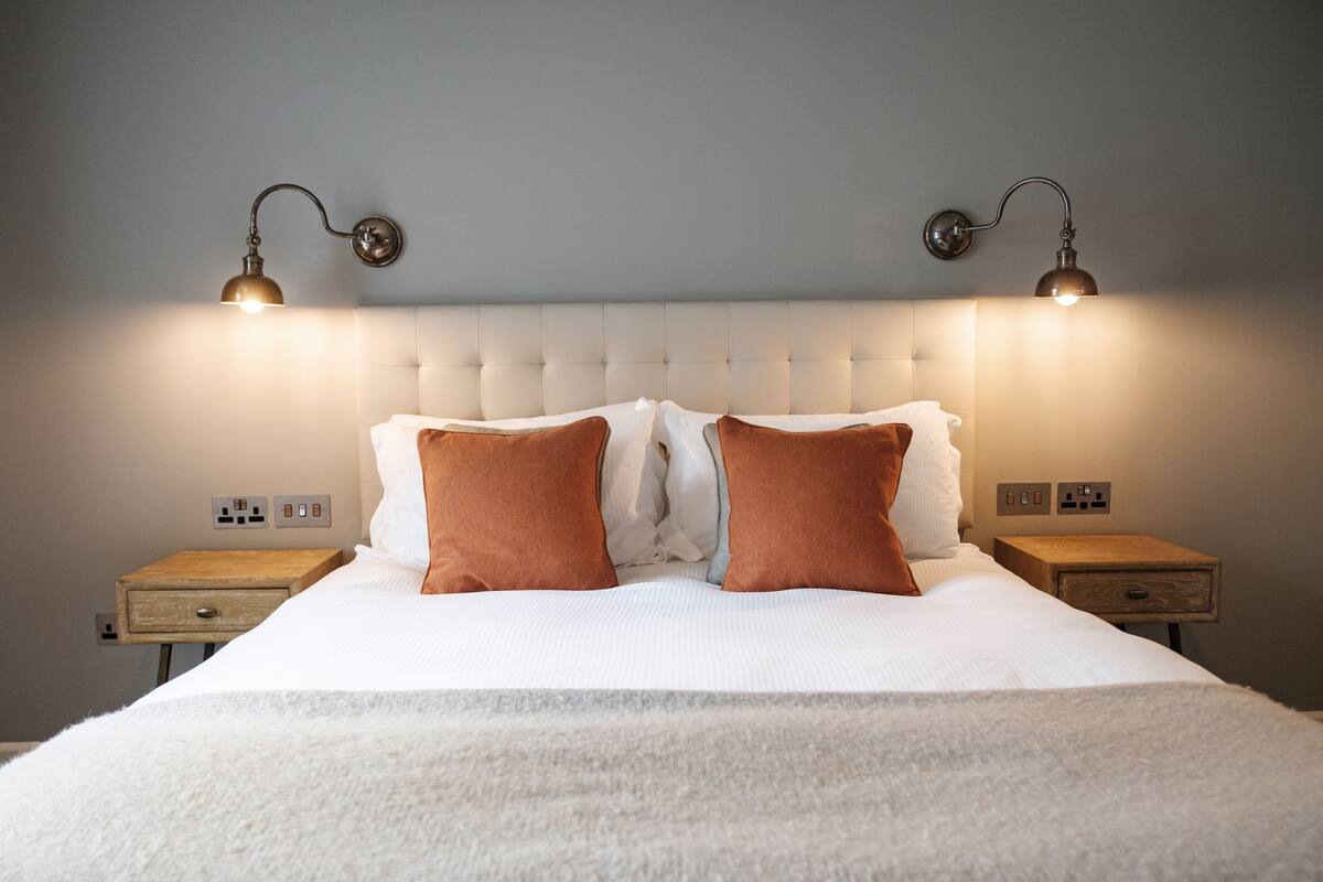 Ein ordentlich bezogenes Bett mit einem geblatteten Kopfteil, zwei Nachttischen und wandmontierten Leselampen.