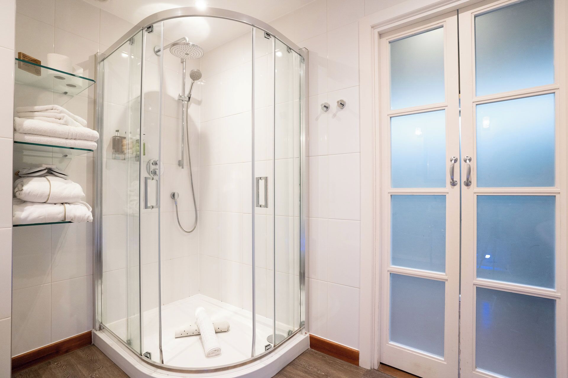 A glass-enclosed shower with a handheld showerhead and a handheld shower attachment.