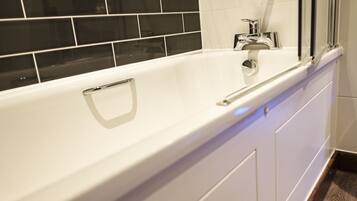 A white bathtub with a chrome faucet and a handrail, set against a black tiled wall.