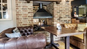 A cozy living area with a brick fireplace, leather seating, and a wooden table. - The Princess Royal (Farnham)