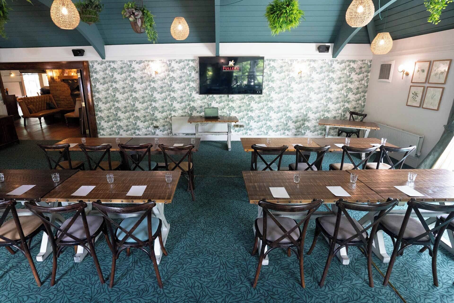 A restaurant with a cozy interior, featuring wooden tables and chairs, a flat-screen TV mounted on the wall, and decorative plants hanging from the ceiling.