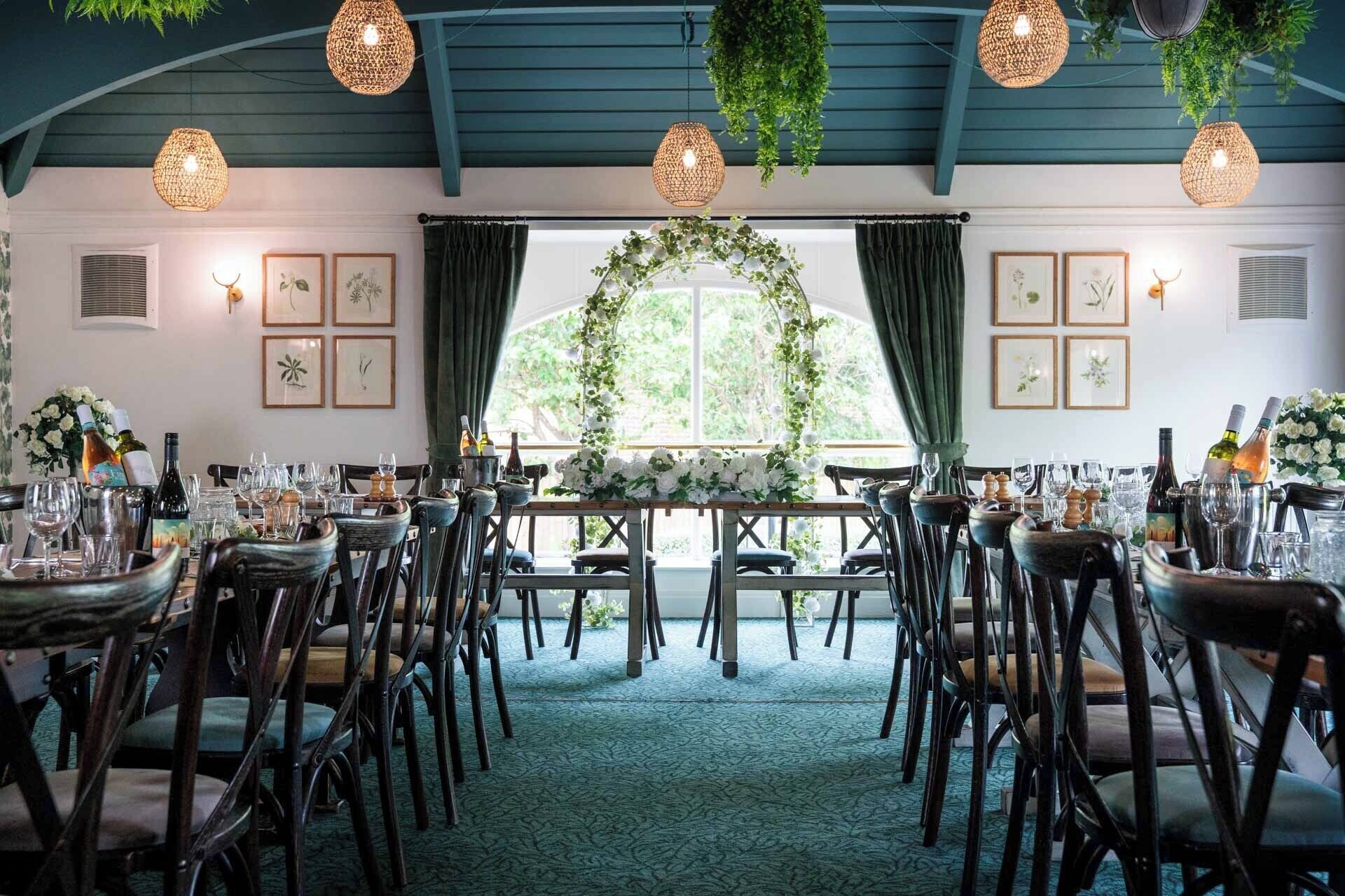 A dining area with tables set for a meal, surrounded by chairs, and decorated with hanging plants and framed pictures.