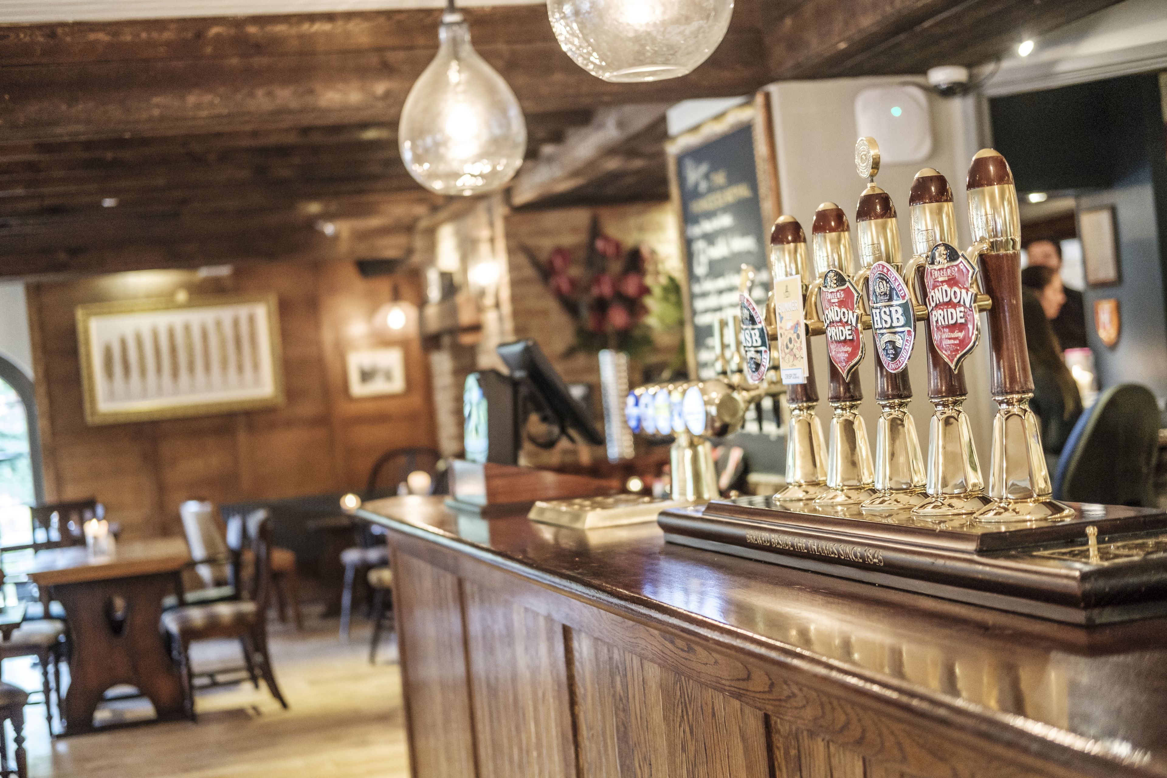 Een bar met houten lambrisering, een toonbank met biertappunten en hangende lampen.