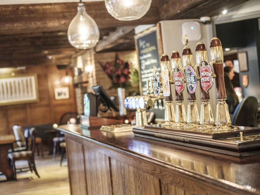 Una zona de bar con paneles de madera, una barra con grifos de cerveza y lámparas colgantes.