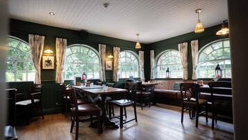 A restaurant with wooden tables and chairs, large arched windows, and hanging pendant lights.