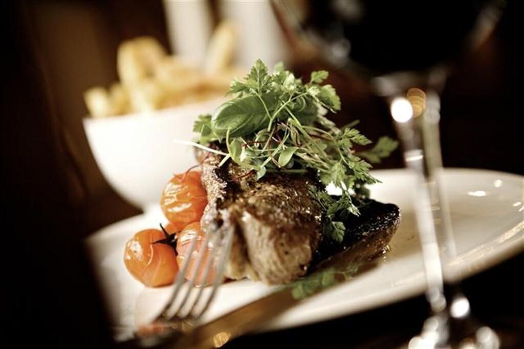 A plate with a steak, cherry tomatoes, and a garnish of greens.